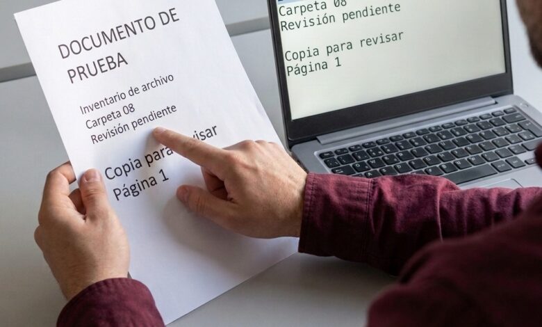 Una persona compara un documento de prueba en papel con las mismas líneas de texto en un portátil